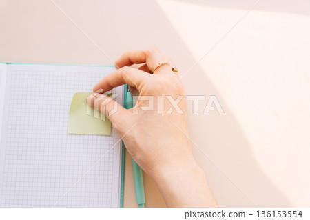 Hand placing sticky note on grid notebook, productivity and organization concept Hand placing sticky note on grid notebook, productivity and organization concept 136153554