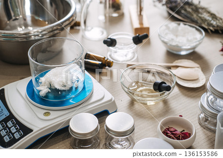Glass beaker with solid oil sits on digital scale surrounded by laboratory equipment and ingredients. Custom oil blending, bespoke facial oils, personalized skincare routine, targeted beauty oils. 136153586