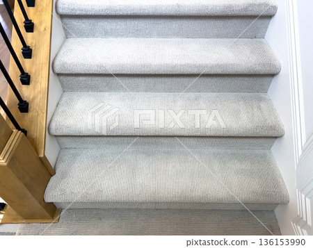 A set of light gray carpeted stairs with white trim and a wooden handrail featuring black metal spindles. Ideal for real estate, interior design, and home renovation visuals. 136153990