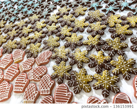 Snowflake and mitten shaped cookies decorated with gold and white icing are arranged together. The mix creates a rich holiday baking scene. 136153991