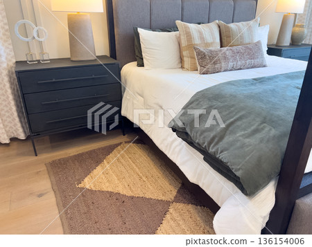 Side view of a contemporary bed with white linens, olive accents, and decorative pillows, set beside a dark wood nightstand with a modern lamp. Side view of a contemporary bed with white linens, olive accents, and decorative pillows, set beside a dark wood nightstand with a modern lamp. 136154006