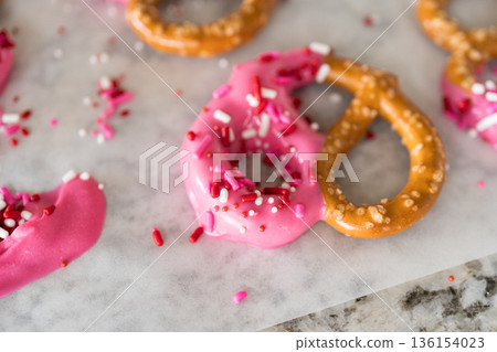 Freshly dipped and still glistening, these crunchy pretzels are lovingly adorned with pink chocolate and a scattering of colorful sprinkles, promising a feast for the senses. 136154023
