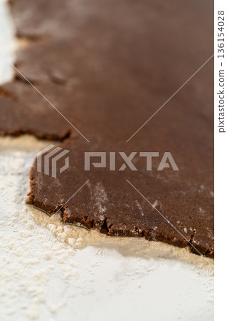 Chocolate cookie dough lies rolled out on a light marble surface dusted with flour. Natural light emphasizes the contrast between the dark dough and pale background. The composition is simple and Chocolate cookie dough lies rolled out on a light marble surface dusted with flour. Natural light emphasizes the contrast between the dark dough and pale background. The composition is simple and 136154028