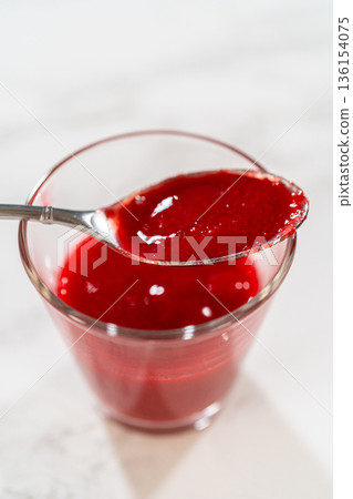 Overhead view of a spoon above a glass filled with raspberry buttercream, ideal for food styling and recipe blog visuals. Especially fitting for Easter Cookie Sandwich with Raspberry Buttercream. Overhead view of a spoon above a glass filled with raspberry buttercream, ideal for food styling and recipe blog visuals. Especially fitting for Easter Cookie Sandwich with Raspberry Buttercream. 136154075