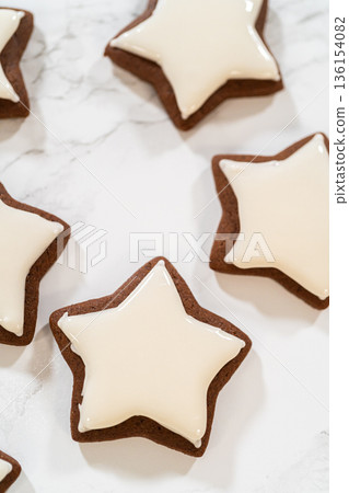 A neat arrangement of gingerbread star cookies covered in white royal icing, emphasizing their festive and uniform design. A neat arrangement of gingerbread star cookies covered in white royal icing, emphasizing their festive and uniform design. 136154082