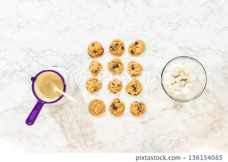Baked cookies are arranged on a marble surface with icing tools nearby. Bright overhead lighting highlights preparation for decorating. 136154085