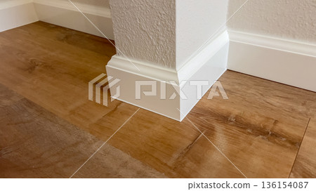A white baseboard wraps around the corner of a wall where it meets a hardwood floor. The surface is clean and sharply defined. 136154087
