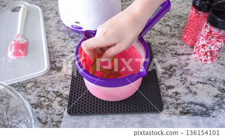 With focused attention, this budding culinary artist dips pretzels into a pot of melted chocolate, creating sweet delights in the warmth of a well-lit home kitchen. 136154101