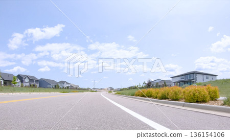 A quiet suburban street in Castle Rock, Colorado with a landscaped median featuring low shrubs. Homes are visible on both sides under a sunny sky. 136154106