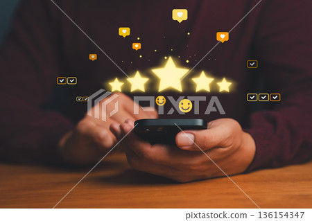 Customer hand using smartphone giving 5 star rating with smiley icons, representing positive feedback, high satisfaction, and excellent service review for online business or digital marketing concept. 136154347