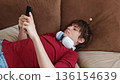Close-up view of a Sad, melancholic teenager using his phone. guy scrolls through social media while lying on the couch. 136154639