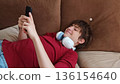 Close-up view of a Happy guy using his phone. happy teenager scrolls through social media while lying on the couch. 136154640