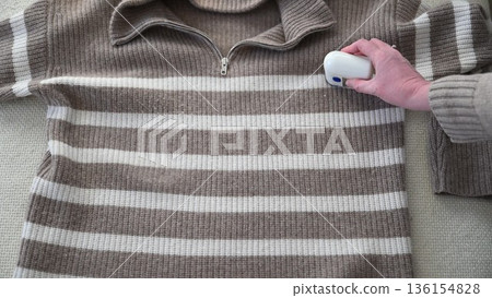 Woman using electric fabric shaver to remove pills from striped sweater at home Woman using electric fabric shaver to remove pills from striped sweater at home 136154828