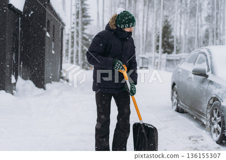 man shoveling snow with a shovel on the driveway of his countryside property during a snowfall 136155307