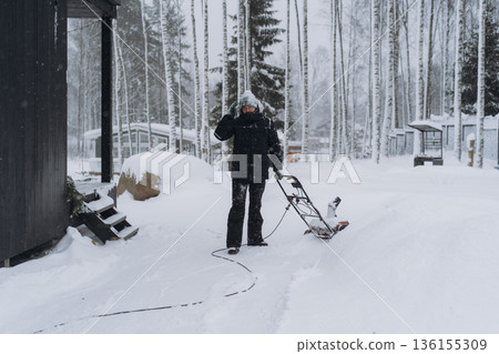 man clearing snowin countryside using electric snow blower 136155309