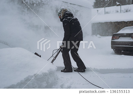 man clearing snowdrifts in countryside using electric snow blower man clearing snowdrifts in countryside using electric snow blower 136155313