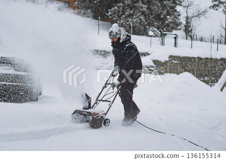man clearing snowdrifts in countryside using electric snow blower man clearing snowdrifts in countryside using electric snow blower 136155314