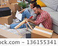 Young couple, boxes aplenty, construct modern wooden shelf furniture in their new apartment, enhancing their home's ambiance 136155341
