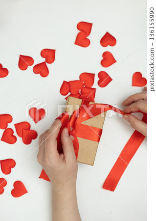 Gift Wrapping for Valentine's Day With Red Ribbon and Heart Decorations on a White Table Gift Wrapping for Valentine's Day With Red Ribbon and Heart Decorations on a White Table 136155990