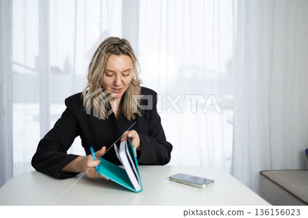 Business Woman Writes in Diary While Sitting at Table by a Window on a Snowy Day Business Woman Writes in Diary While Sitting at Table by a Window on a Snowy Day 136156023