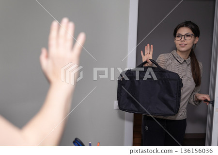 Young Professional Leaving for Work Waving Goodbye Near Doorway Young Professional Leaving for Work Waving Goodbye Near Doorway 136156036