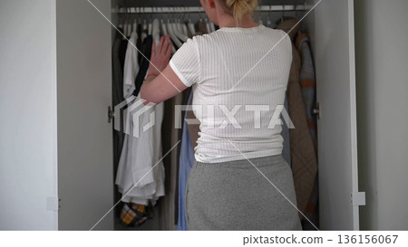 Woman choosing clothes from wardrobe while organizing capsule closet at home 136156067