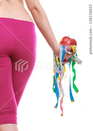 Closeup of woman holding apple and tape measures. Closeup of woman holding apple and tape measures. 136156825