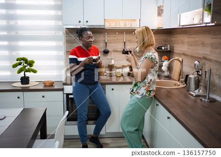Friends enjoying a warm drink together in a cozy modern kitchen 136157750