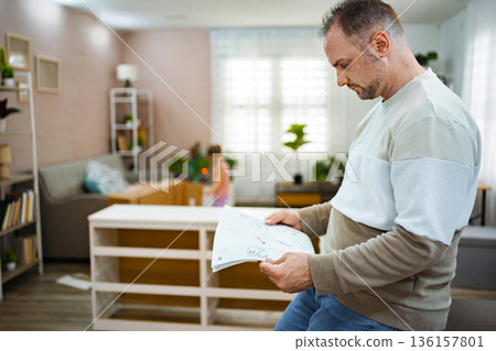 Man follows instructions to assemble furniture in cozy room 136157801
