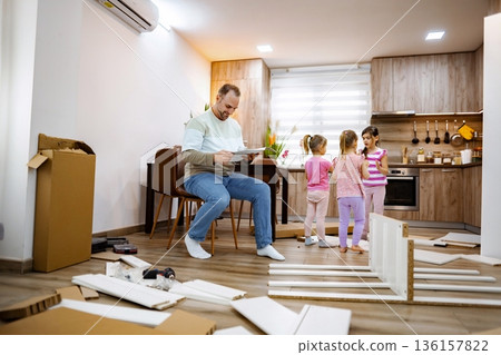 Father engages with children while assembling furniture in the kitchen Father engages with children while assembling furniture in the kitchen 136157822