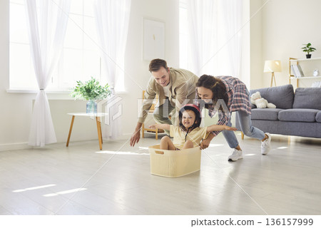 Happy parents push toddler in basket at home, playful family time in living room 136157999