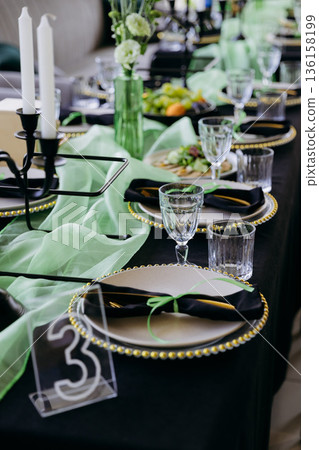 Elegant black and green tablescape with candles, place settings and glassware Elegant black and green tablescape with candles, place settings and glassware 136158199