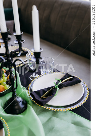 Luxury black-green tablesetting with gold cutlery and beaded charger in sunlight 136158203