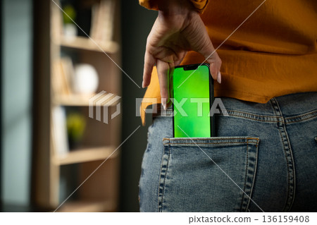 Unrecognizable woman slipping a modern smartphone with green screen into her jeans back pocket, close-up lifestyle shot ideal for mockups, tech, app and advertising concepts Unrecognizable woman slipping a modern smartphone with green screen into her jeans back pocket, close-up lifestyle shot ideal for mockups, tech, app and advertising concepts 136159408