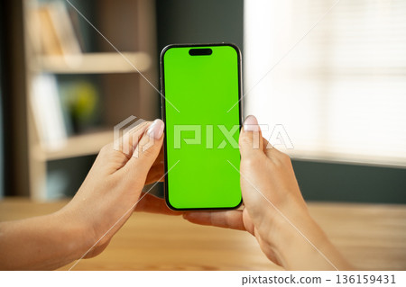 Woman holding a modern smartphone with a vivid green screen display, perfect for showcasing content, applications, or websites with a customizable chroma key background for creative projects 136159431