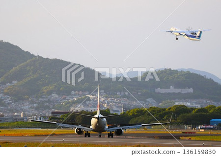 一架飛機正在大阪伊丹機場的跑道上降落，其他飛機則在其上方飛過。 136159830