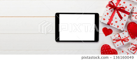 Digital tablet blank screen with gift box and hearts decor on wooden table. Top view. Valentines Day concept background Digital tablet blank screen with gift box and hearts decor on wooden table. Top view. Valentines Day concept background 136160049