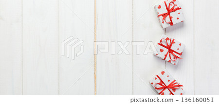Valentine or other holiday handmade present in paper with red hearts and gifts box in holiday wrapper. Present box gift on white wooden table top view with copy space, empty space for design Valentine or other holiday handmade present in paper with red hearts and gifts box in holiday wrapper. Present box gift on white wooden table top view with copy space, empty space for design 136160051