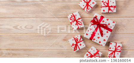 Valentine or other holiday handmade present in paper with red hearts and gifts box in holiday wrapper. Present box of gift on orange wooden table top view with copy space, empty space for design 136160054