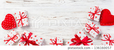 Valentine or other holiday handmade present in paper with red hearts and gifts box in holiday wrapper. Present box of gift on white wooden table top view with copy space, empty space for design Valentine or other holiday handmade present in paper with red hearts and gifts box in holiday wrapper. Present box of gift on white wooden table top view with copy space, empty space for design 136160057
