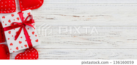 Valentine or other holiday handmade present in paper with red hearts and gifts box in holiday wrapper. Present box of gift on white wooden table top view with copy space, empty space for design Valentine or other holiday handmade present in paper with red hearts and gifts box in holiday wrapper. Present box of gift on white wooden table top view with copy space, empty space for design 136160059