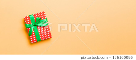 Gift box with green bow for Christmas or New Year day on orange background, top view with copy space Gift box with green bow for Christmas or New Year day on orange background, top view with copy space 136160096