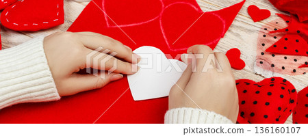 women's hands make red hearts from the fabric. Preparation for St. Valentine's Day. homemade festive decorations. Above view, flat lay 136160107