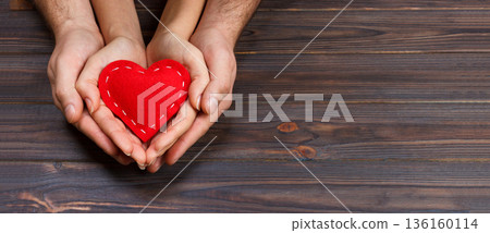 Love, family concept. Close up of man and woman hands holding red rubber heart together Love, family concept. Close up of man and woman hands holding red rubber heart together 136160114