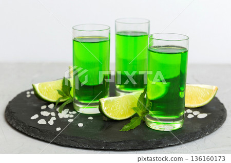 Sweet refreshing mint liqueur, with ice and mint leaves on table background, Shots with lime slice and mint flat lay 136160173