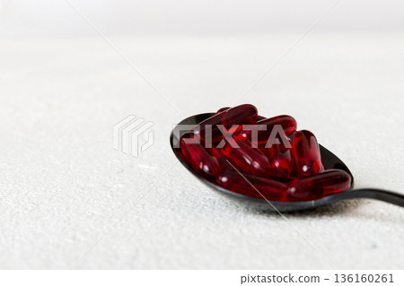 Vitamin capsules in a spoon on a colored background. Pills served as a healthy meal. Red soft gel vitamin supplement capsules on spoon 136160261