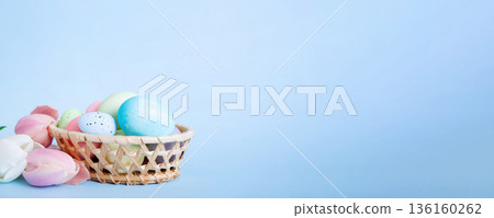 Happy Easter composition. Easter eggs in basket on colored table with yellow Tulips. Natural dyed colorful eggs background with copy space 136160262