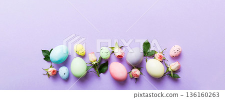 Happy Easter. Easter eggs on colored table with yellow roses. Natural dyed colorful eggs background top view with copy space Happy Easter. Easter eggs on colored table with yellow roses. Natural dyed colorful eggs background top view with copy space 136160263