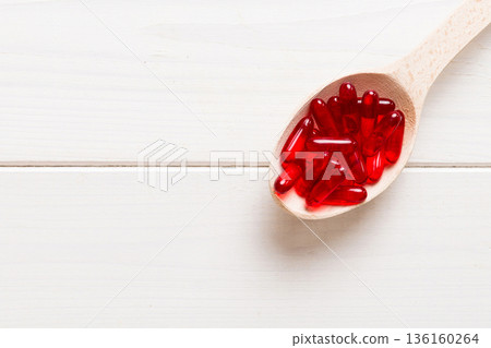 Vitamin capsules in a spoon on a colored background. Pills served as a healthy meal. Red soft gel vitamin supplement capsules on spoon Vitamin capsules in a spoon on a colored background. Pills served as a healthy meal. Red soft gel vitamin supplement capsules on spoon 136160264