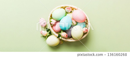 Happy Easter. Easter eggs in basket on colored table with yellow roses. Natural dyed colorful eggs background top view with copy space 136160268